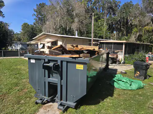Rear view of a full All Waste Dumpsters container of patio lumber below the maximum load level sticker under moss covered oaks in Summerfield
