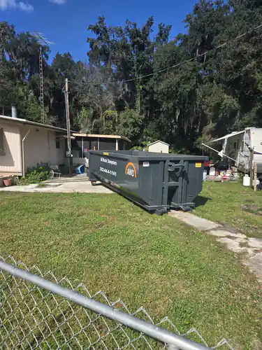Empty All Waste Dumpsters container on the side lawn of a Summerfield home beside a concrete walk, with a chain link fence in the foreground
