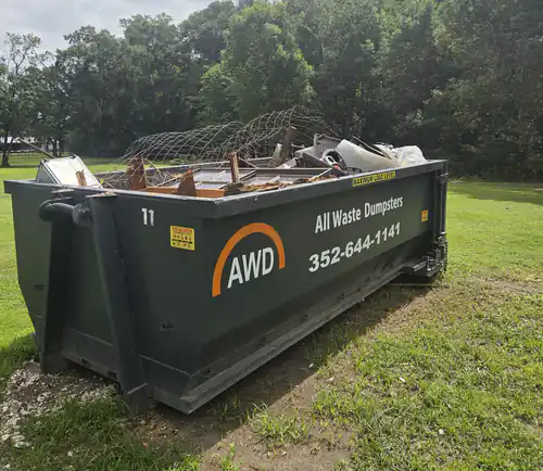 All Waste Dumpsters container number 11 in a grassy Ocala yard with wire fencing and scrap wood piled over the side rail