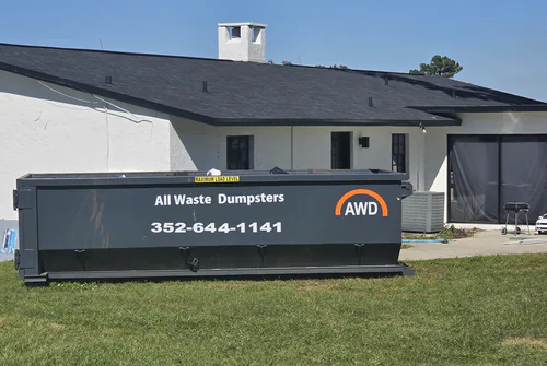 All Waste Dumpsters 20 yard container on the grass beside a white stucco home with a dark shingle roof in Ocala