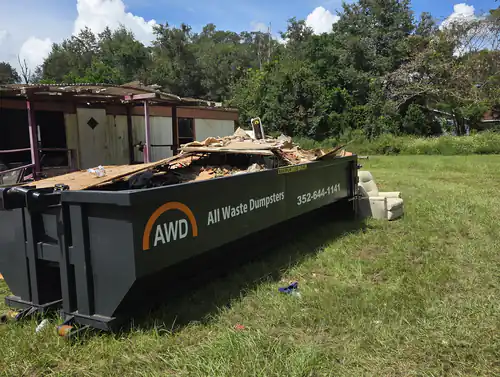 All Waste Dumpsters container on an Ocala lawn loaded above the maximum load level with lumber and drywall, with a recliner beside it