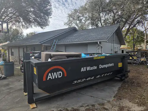Full All Waste Dumpsters 25 yard container on wood blocks in the driveway of an Ocala home, with a ladder leaning against the garage