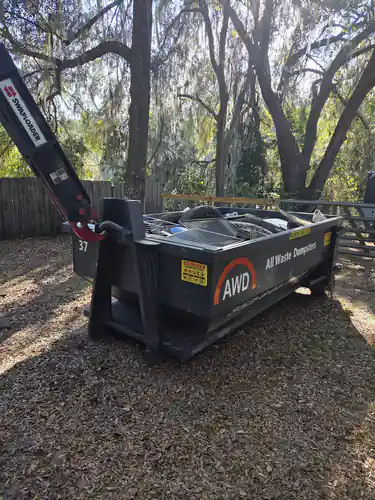 Full All Waste Dumpsters 10 yard container on fallen leaves beside a privacy fence under moss draped oaks in an Ocala backyard