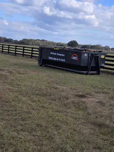 All Waste Dumpsters 20 yard container number 42 loaded with lumber on pasture grass beside a black board fence in Lady Lake