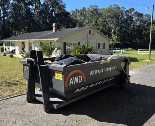 All Waste Dumpsters 10 yard container number 37 loaded with black trash bags in the driveway of a ranch style home in Ocala