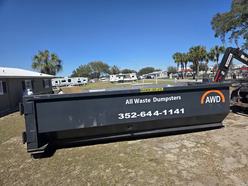 All Waste Dumpsters container on dry grass beside a block service building with a propane tank at an Ocala RV park with travel trailers behind it