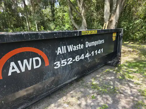Close view of an All Waste Dumpsters 20 yard container on a sandy strip under shade trees in an Ocala backyard