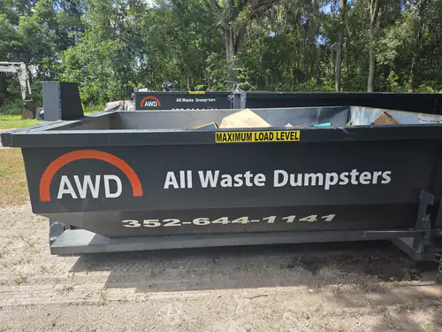Empty All Waste Dumpsters container in the company yard in Ocala with a second container and a mini excavator behind it