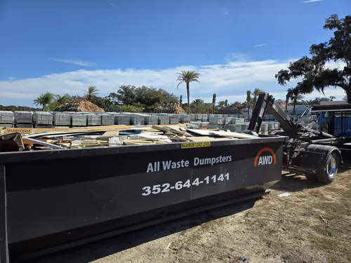 Full All Waste Dumpsters 25 yard container of pallets and packaging at a Belleview paver yard, with the hook lift arm raised for pickup